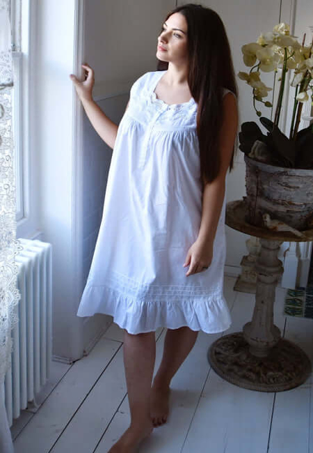 Helen is a shorter length sleeveless cotton nighty, which features wide straps. The straps have decorated lace trim on them, which also runs along the bodice. There are pintucks above the hem which leads down to a flounced hemline. This sleeveless cotton nighty has been designed to give a flared, loose, and comfortable fit. Front opening buttons, also gives the opportunity for this design to be used, as maternity wear or to support mobility.
