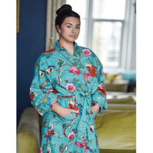 Teal Exotic Flower wraparound cotton dressing gown lighter weight 100% cotton.  Beautiful print of multi-coloured exotic flowers and foliage against a vivid teal background. This cotton dressing gown is embellished with a contrasting sage green pom-pom trim on the cuffs, open front, top of the pockets and it has a long matching waist tie belt.