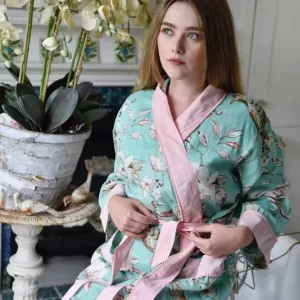 Lightweight Dressing Gown Ladies. This delightful mint blossom dressing gown features birds with soft green plumes sitting on branches budding into cream blooms against a mint background. This dressing gown is edged on the cuffs, open front, and pockets in a contrasting pink cotton with small pom-poms trims and it has a long belt to tie around the waist.  Lightweight cotton, easy and elegant to wear.