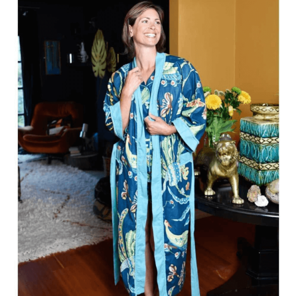 Lightweight cotton dressing gown is so stylish and easy to wear, the wraparound style makes it a comfortable fit for all. The French navy is the perfect backdrop for a print of abstract flowers, leaves, and decorative patterns with exotic birds. The colours in the print include peach, rusty orange, pale blue, and mint green. The dressing gown is embellished with a contrasting sky-blue border with pom-pom trim on the cuffs, open front, and top of the pockets and it has a long matching waist tie belt. This lightweight cotton dressing gown is made from 100% soft breathable cotton and so comfortable to lounge around in.